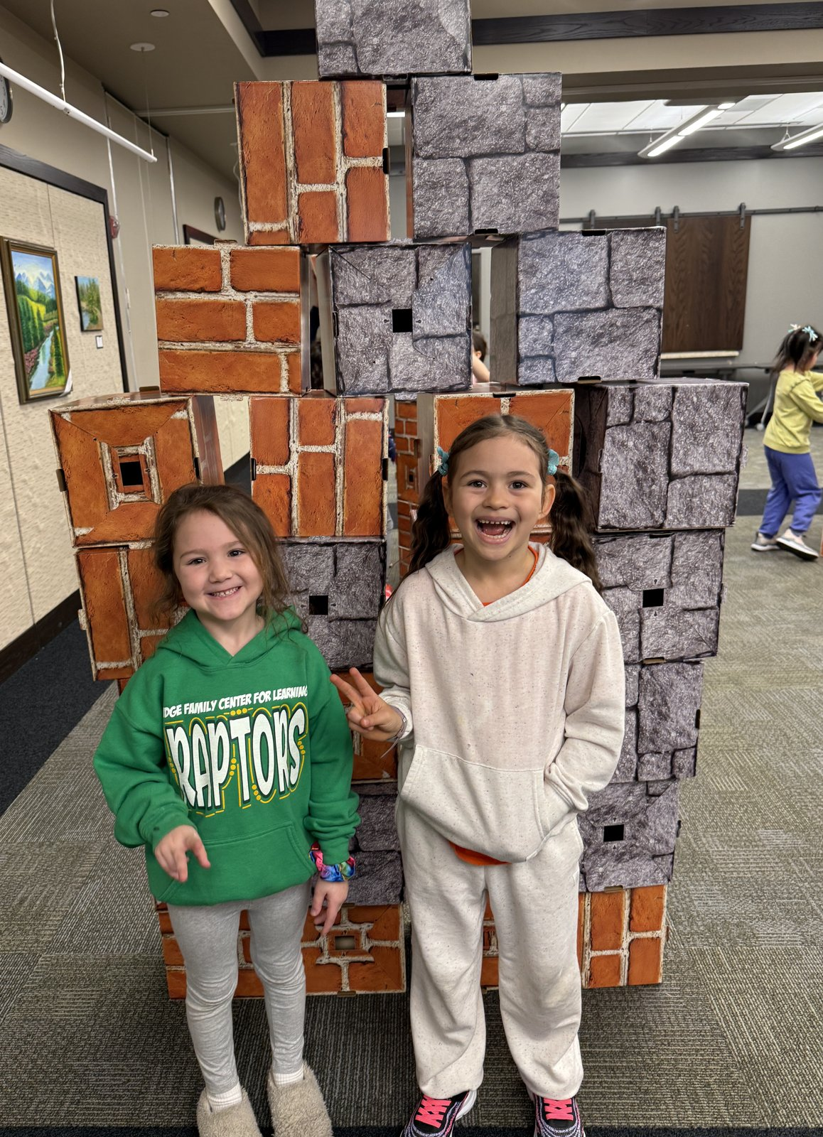 Two children grinning in front of the wall they built