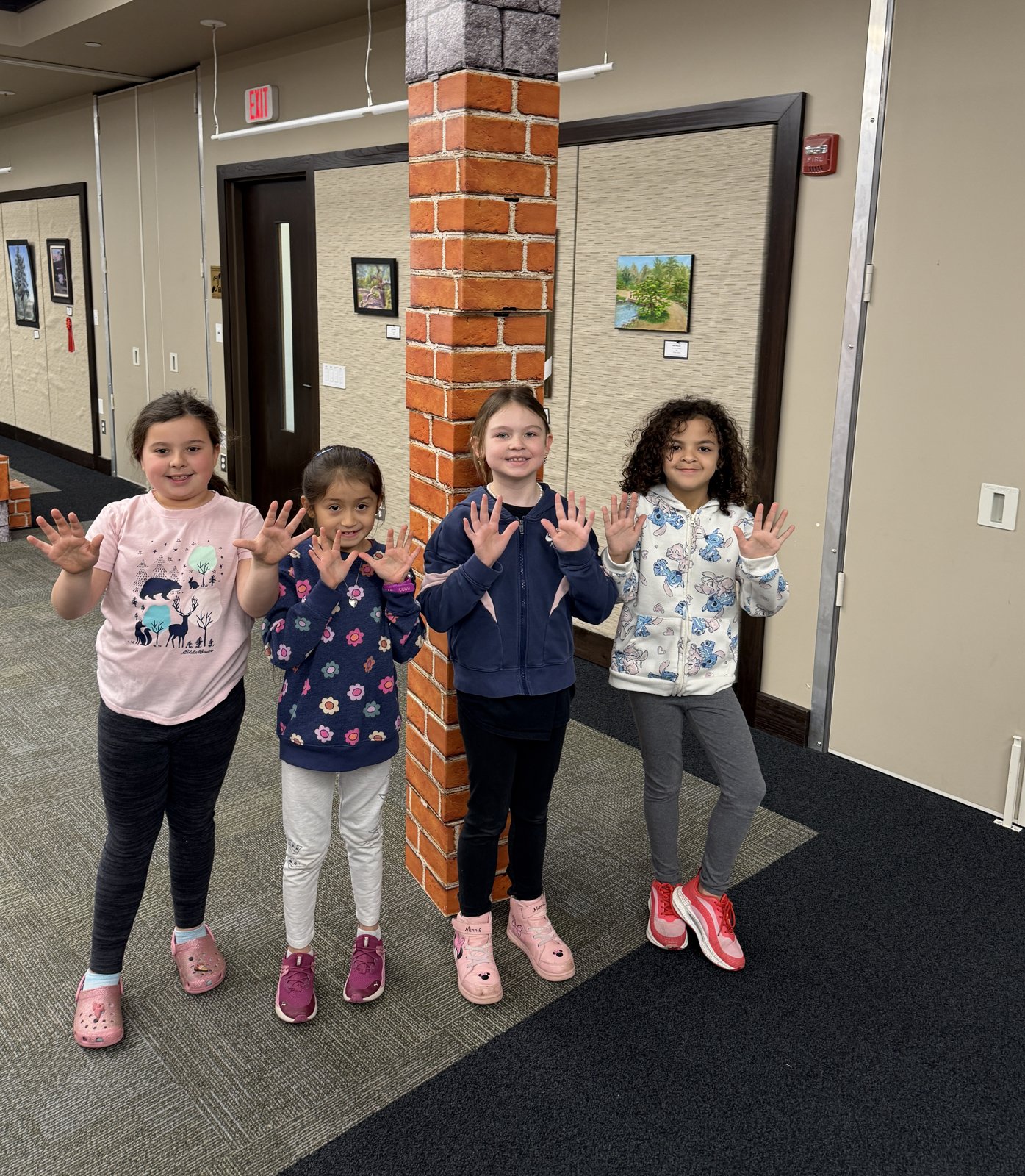 Four children waving beside a tower of giant blocks